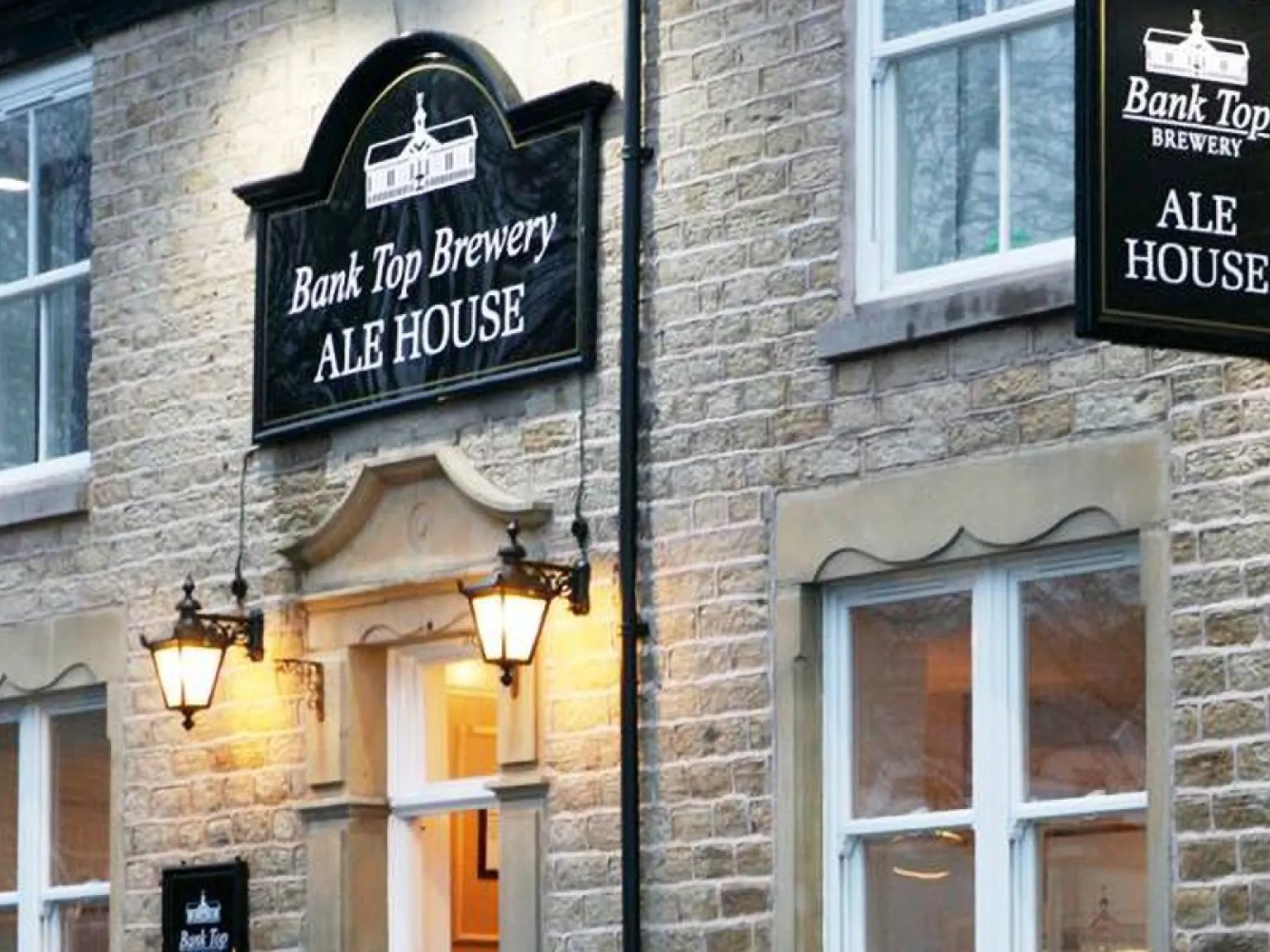 The stone front of the Ale House on Church Street with its lit Bank Top Brewery Ale House signs, a brewery taproom in Horwich