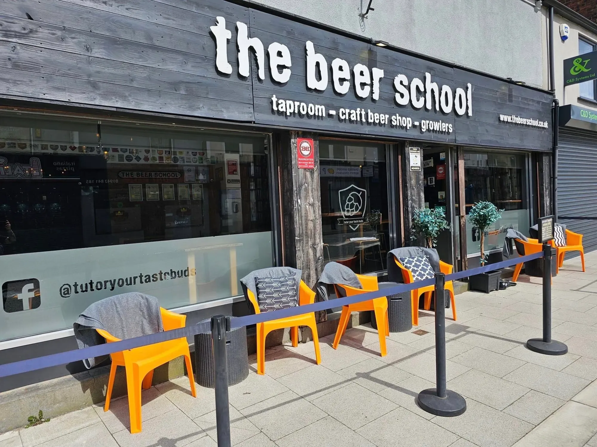 The dark timber front of the Beer School on Market Street with its sign and orange chairs outside, a pub in Westhoughton