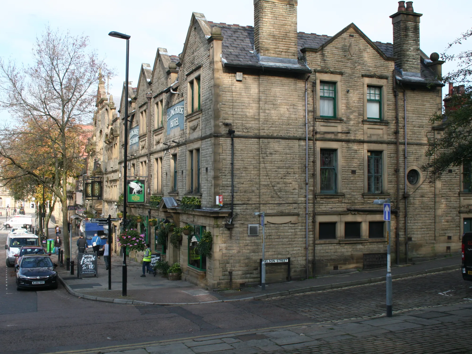 The gabled stone frontage of the Flying Horse Hotel on Packer Street, with its hanging baskets and pub sign, a pub in Rochdale