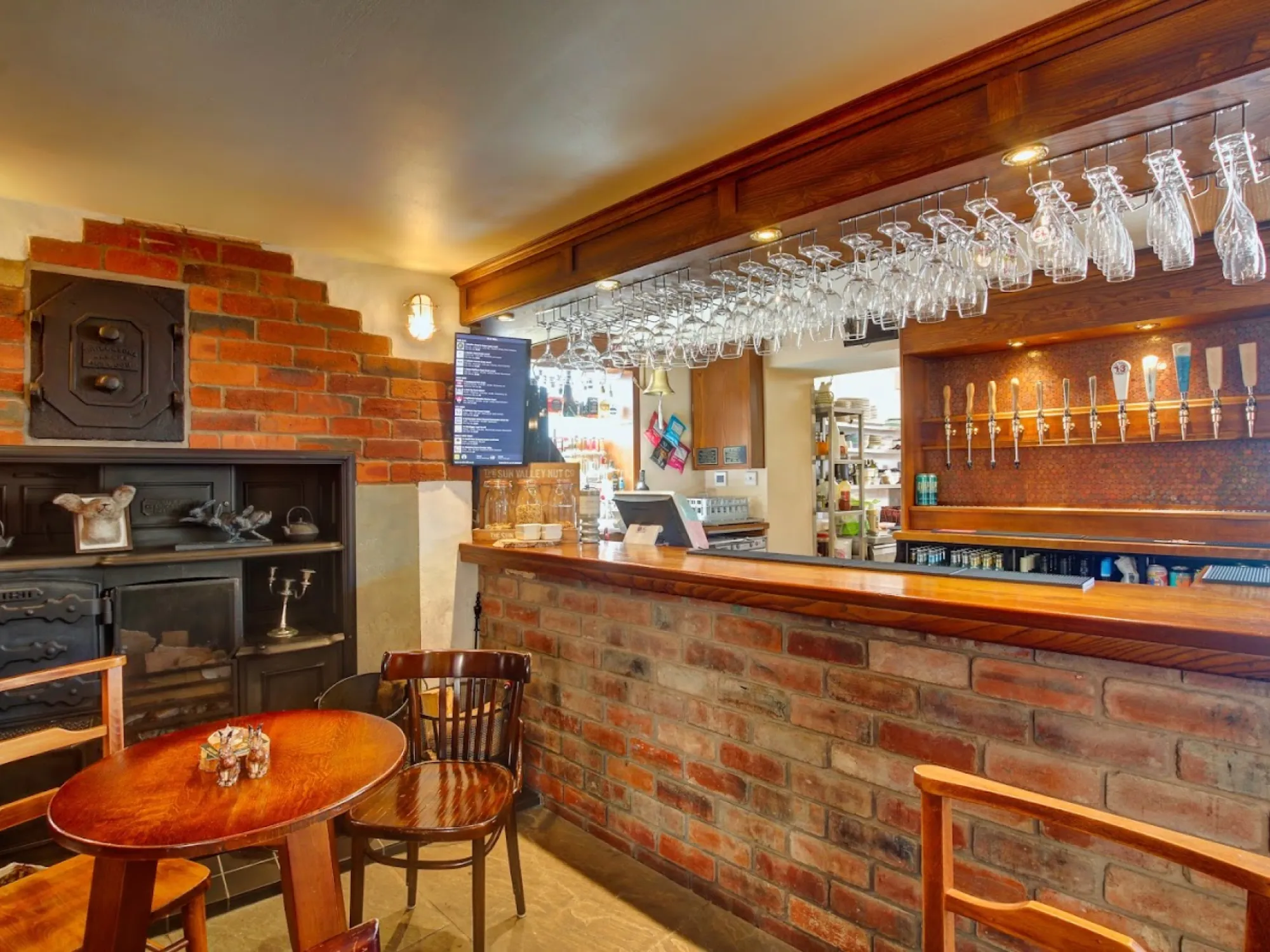 The brick-fronted bar with hanging glasses and the cask pumps, beside an old range and a table and chairs at Hare on the Hill, a pub in Littleborough
