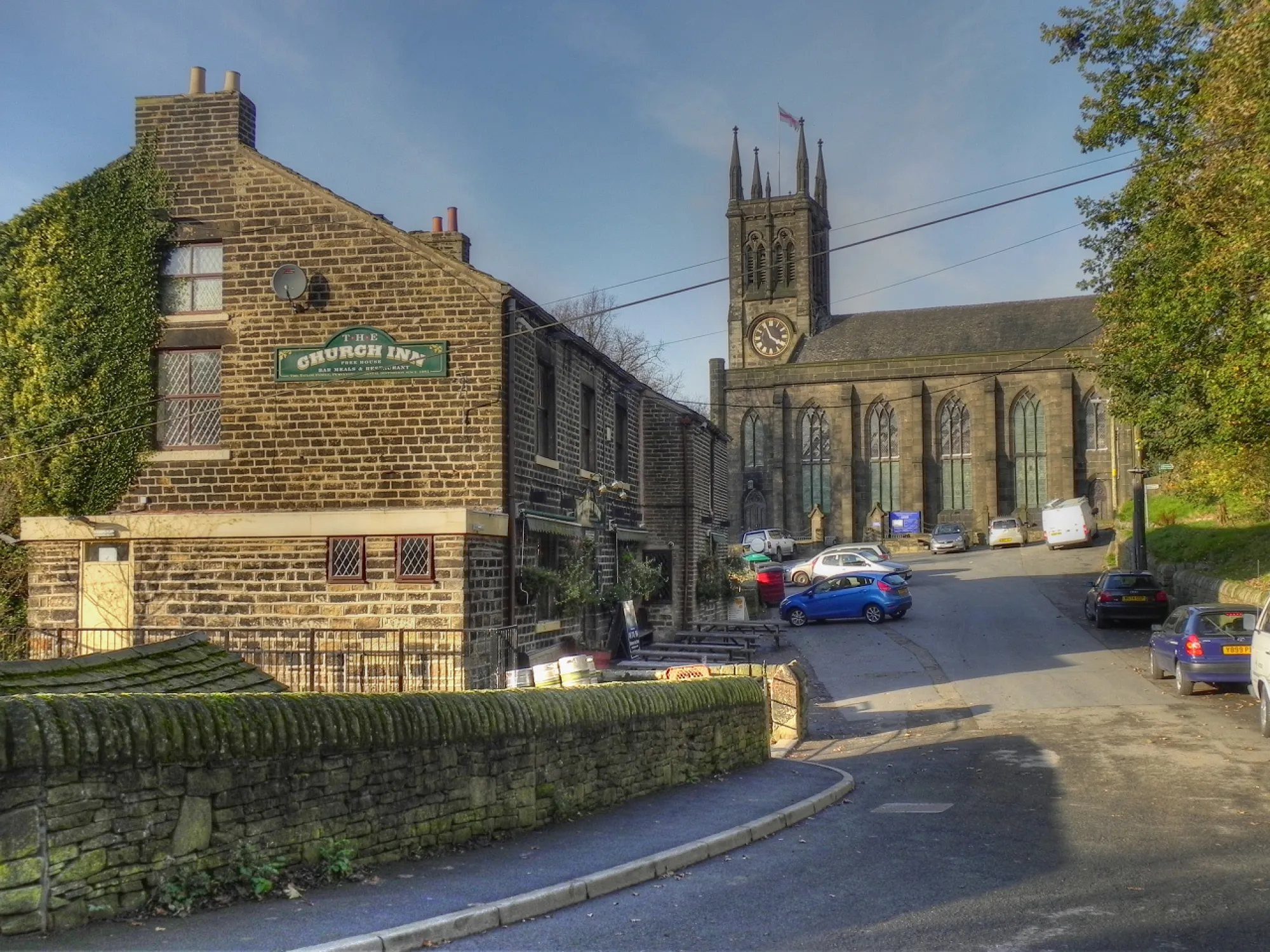 The ivy-clad stone Church Inn with its sign on the gable, St Chad's Church behind it on Church Lane at Church Inn, Uppermill, a brew pub in Uppermill