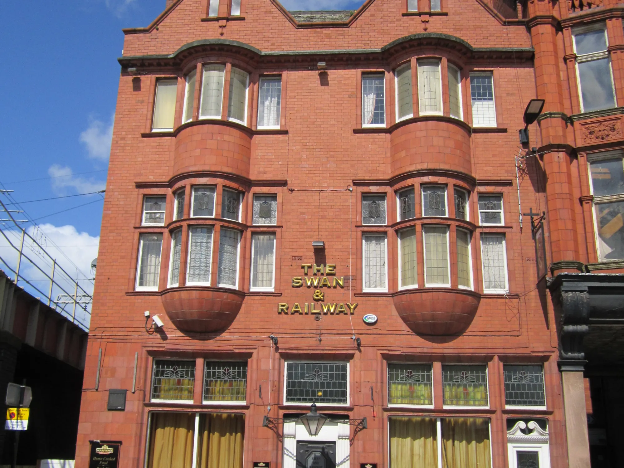 The red brick and terracotta front of the pub on Wallgate, with its name painted between the bay windows at Swan & Railway Hotel, a pub in Wigan