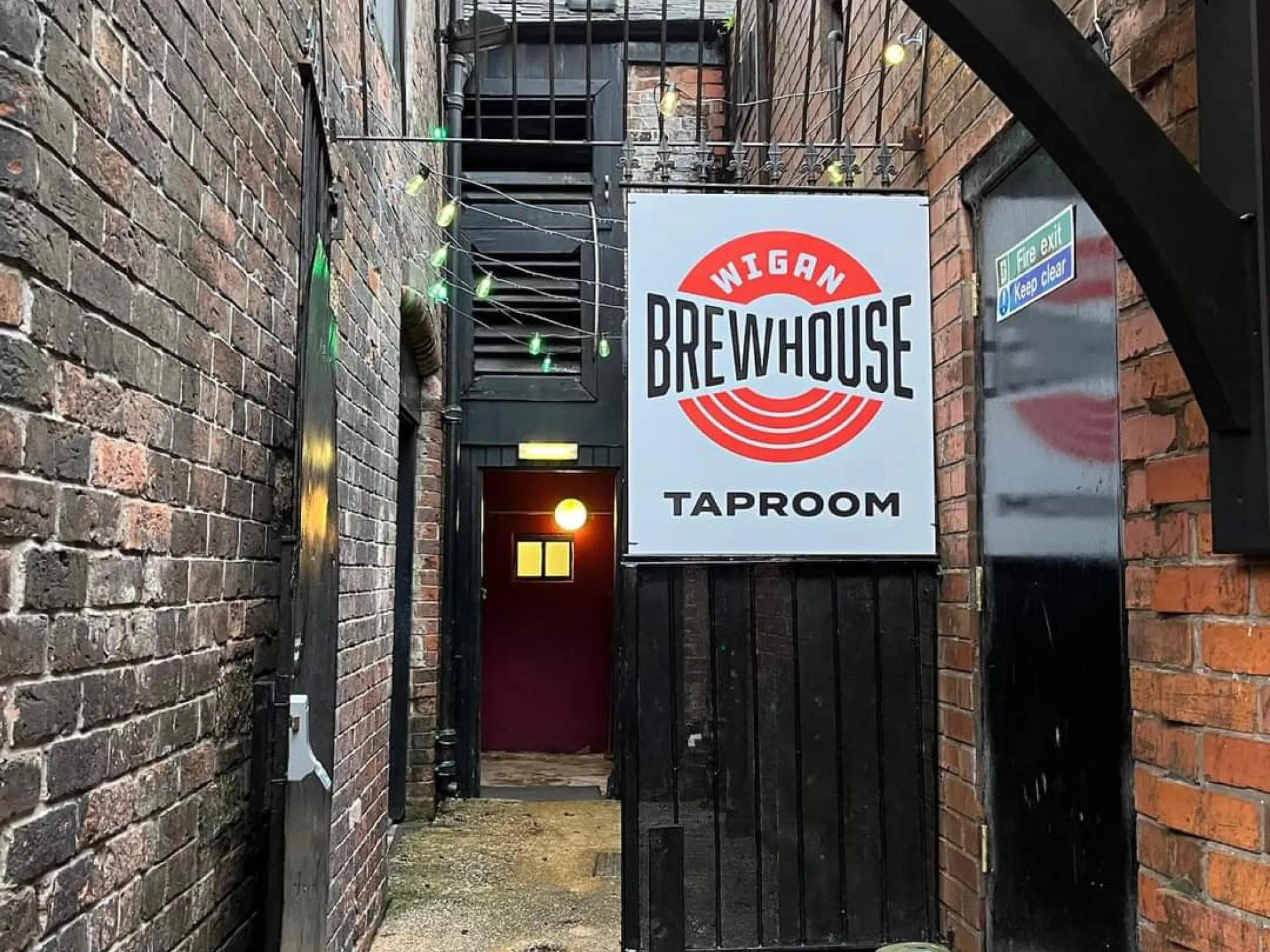 The Wigan Brewhouse Taproom sign hanging over the brick alley entrance off Wallgate, a brewery taproom in Wigan