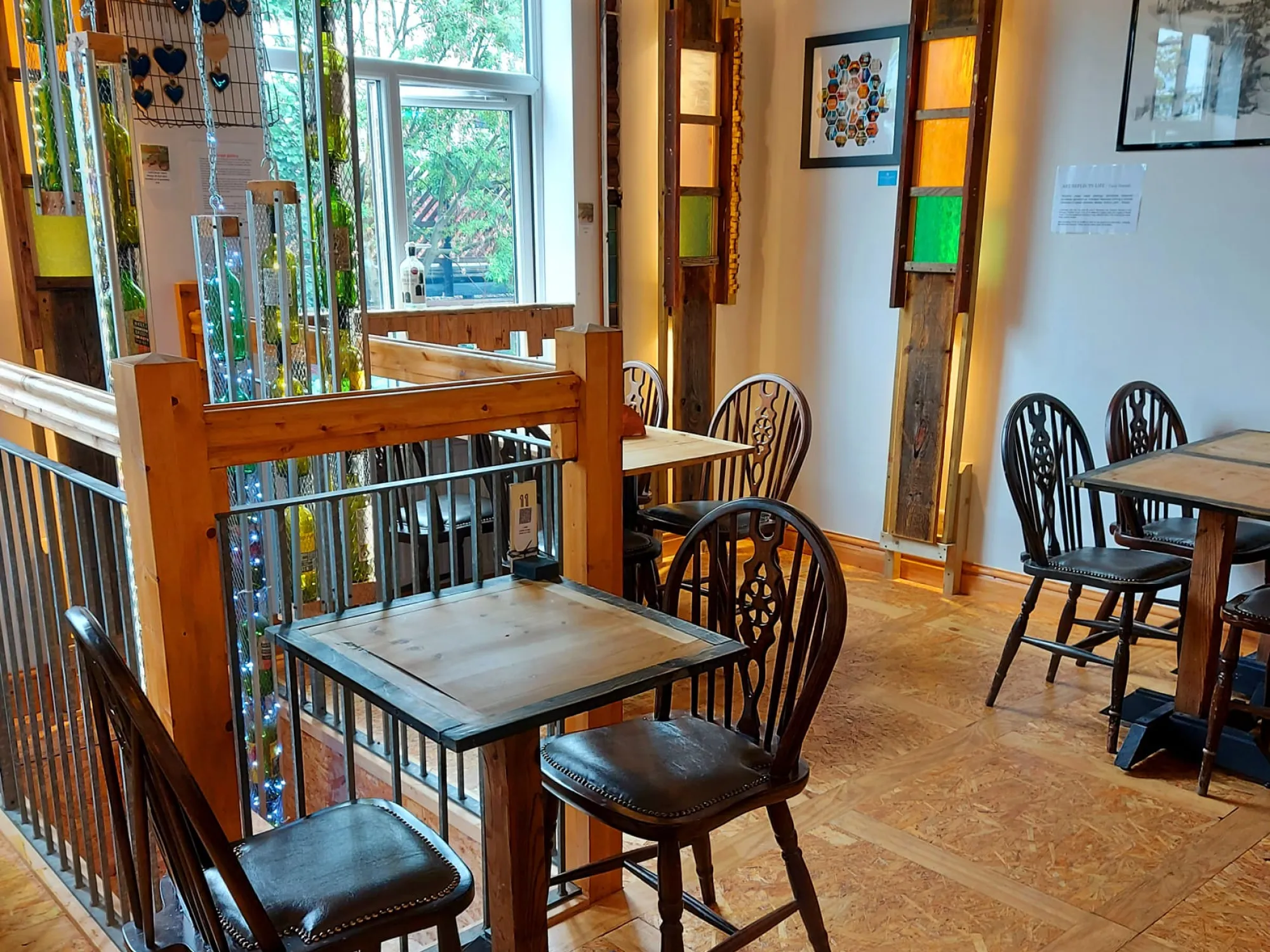 The upstairs seating with wheelback chairs, wooden tables and stained-glass light panels at The Chiverton Tap, a pub in Cheadle Hulme