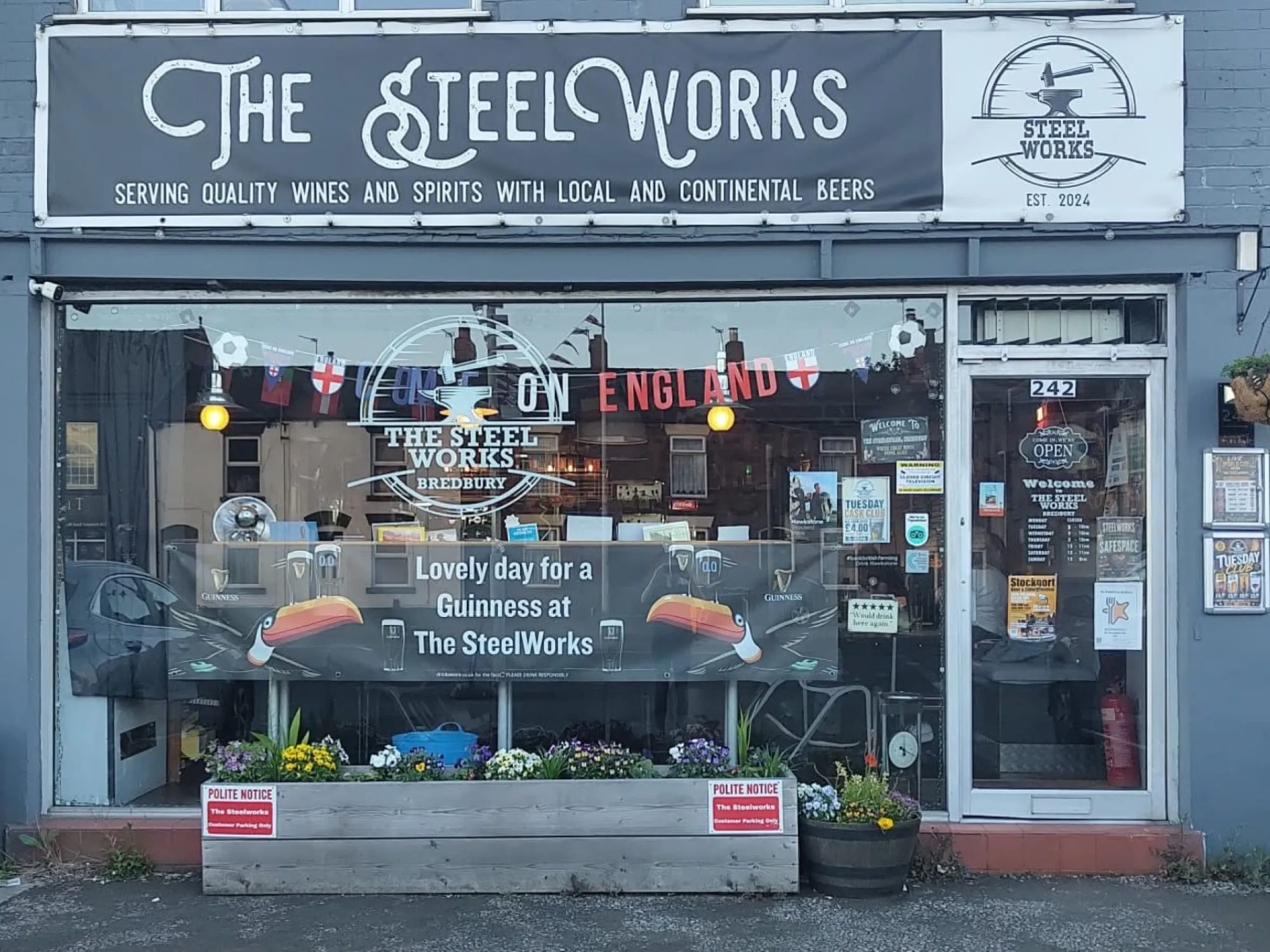 The grey shopfront of The SteelWorks on Stockport Road West, with its sign over the window and planters out front at Steel Works, a pub in Bredbury