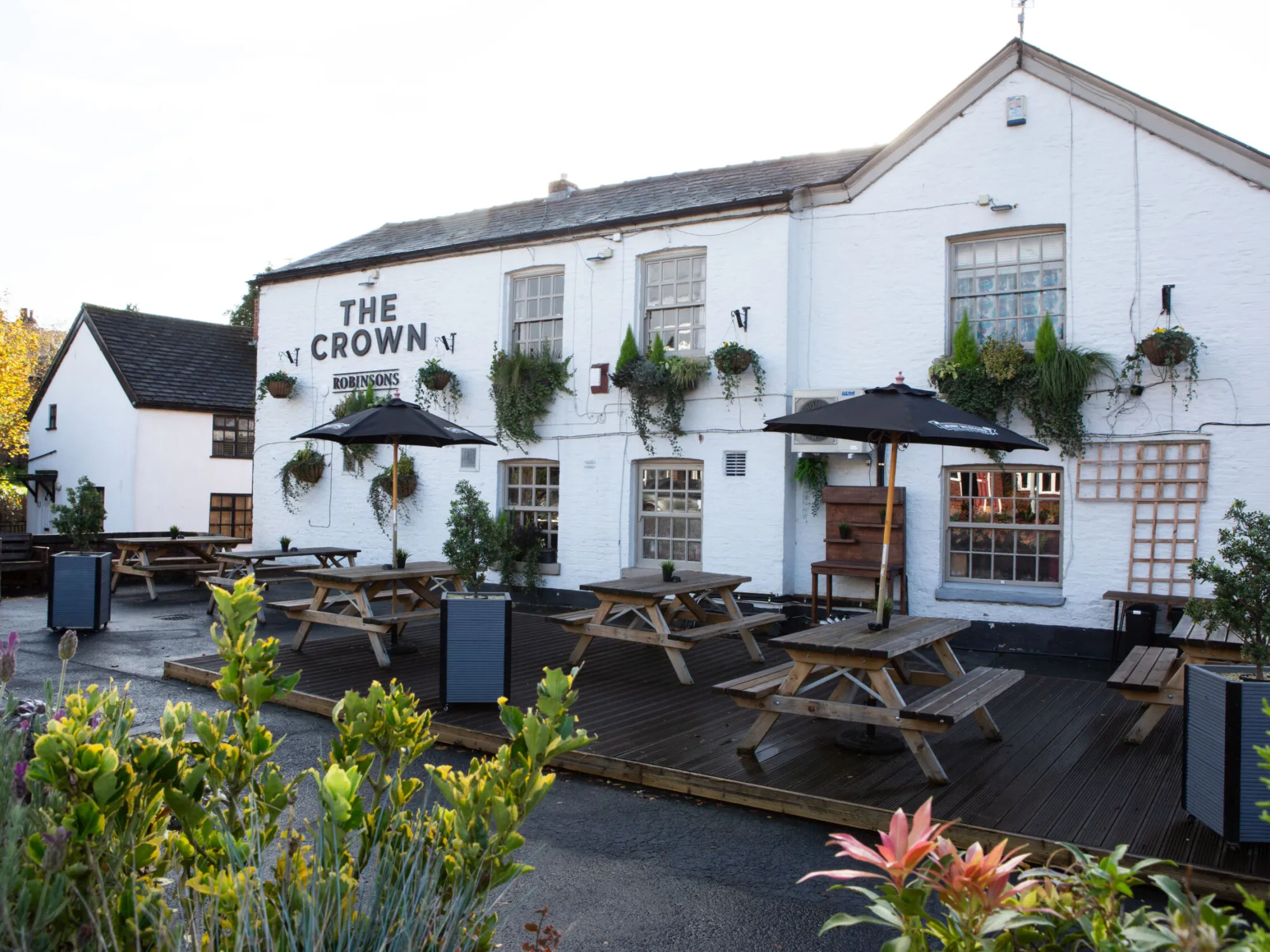 The white-painted front of The Crown with its decked terrace, picnic benches and parasols at The Crown, Heaton Mersey, a pub in Heaton Mersey