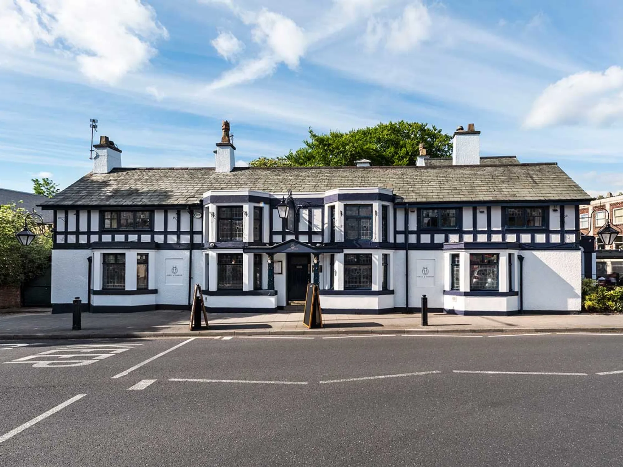 The black and white mock-Tudor front of the Horse & Farrier on Gatley Road under a blue sky, a pub in Gatley