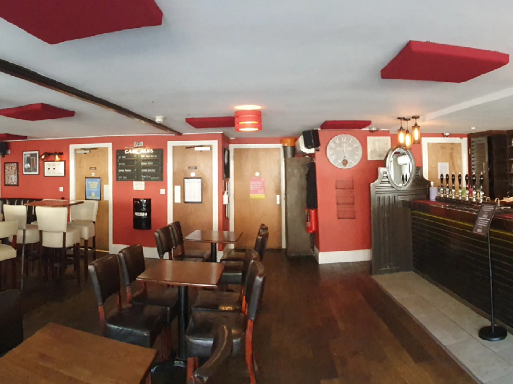 A wide view inside Costello's Bar, with tables and banquettes on the left and the bar and handpumps on the right, a brewery taproom in Altrincham