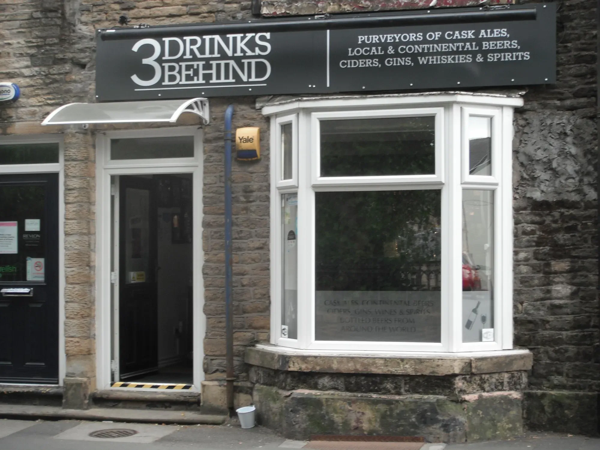 The stone frontage of 3 Drinks Behind on Stockport Road, with its black sign and white bay window, a pub in Hyde