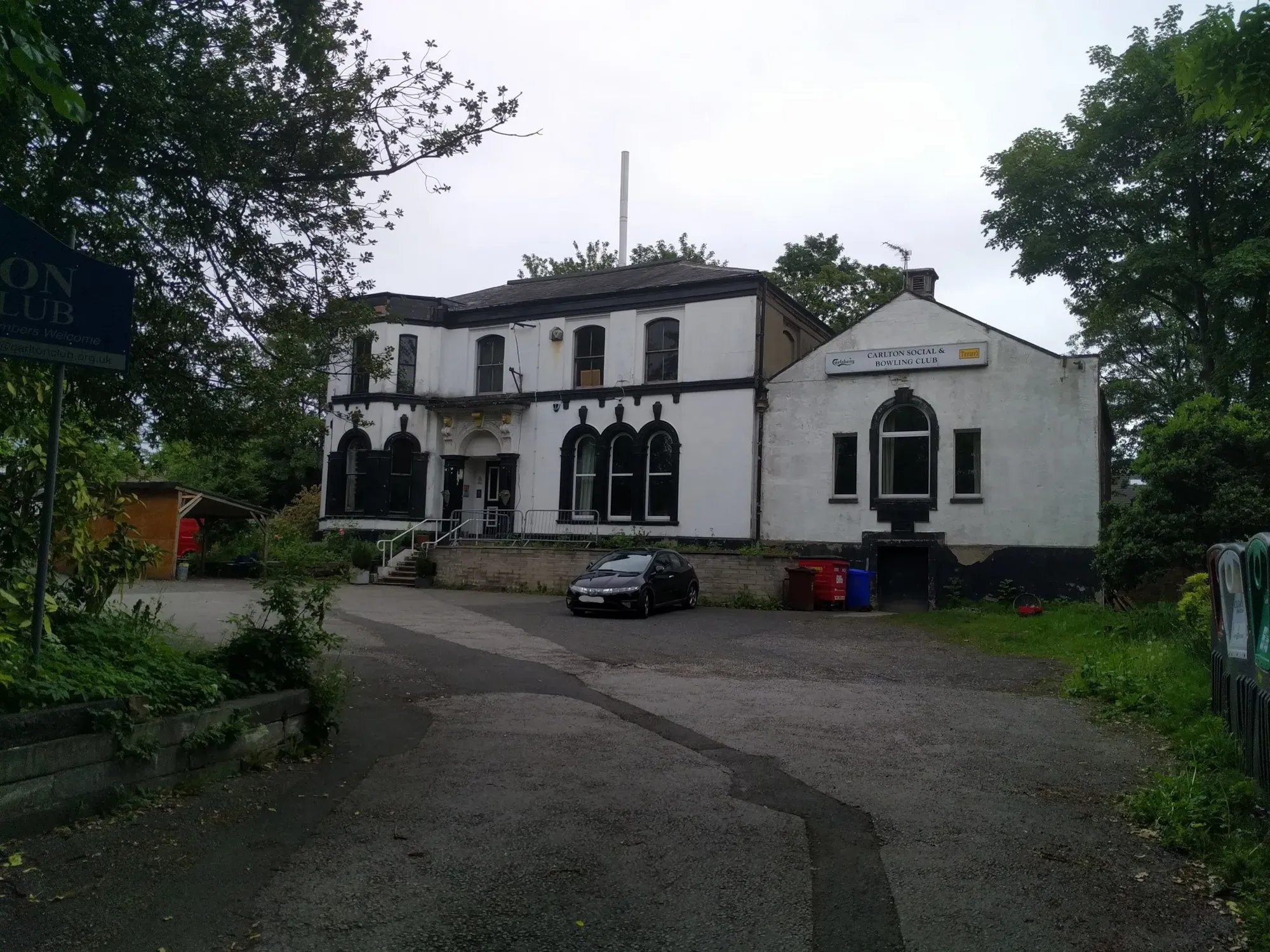The white two-storey Carlton Club building at the end of its drive on Carlton Road, framed by trees, a craft beer bar in Whalley Range