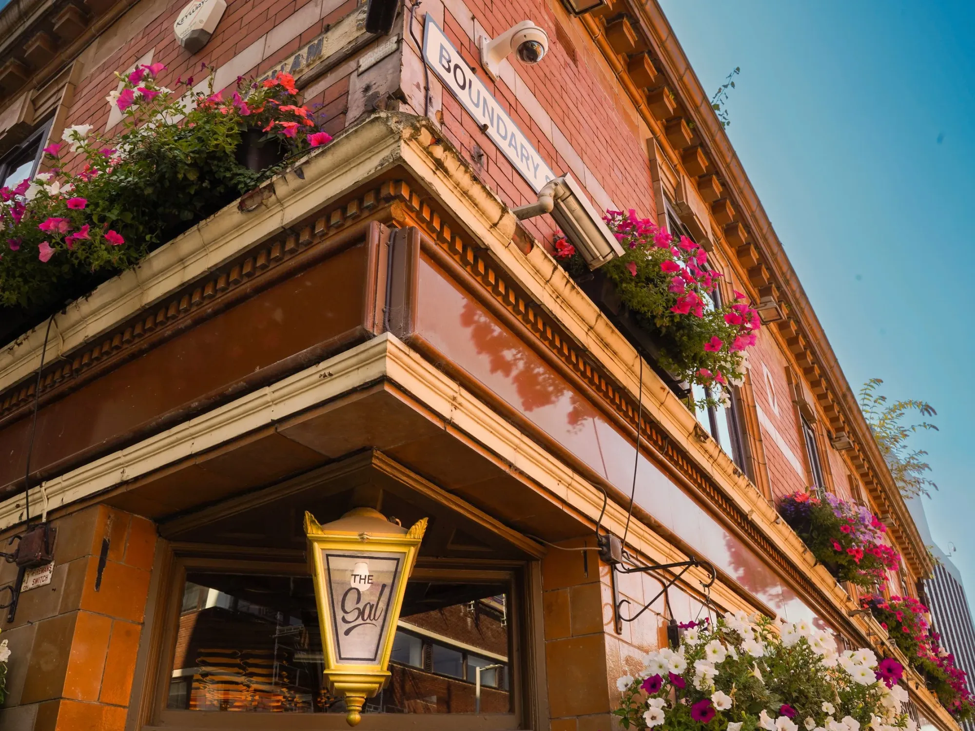 The tiled corner of the Sal on Higher Chatham Street, with its lantern sign and hanging flower boxes at The Salutation, a pub in Hulme