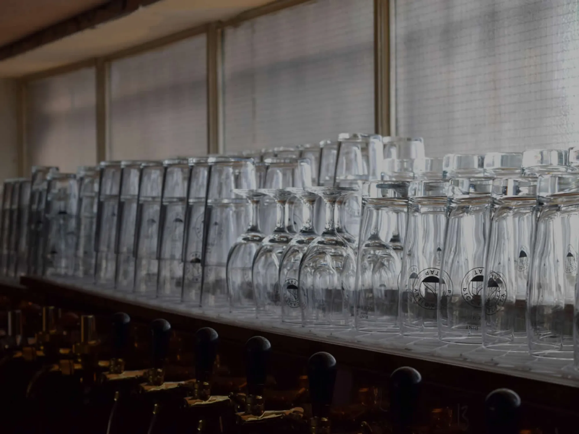 Branded glasses stacked on the back bar above a row of beer taps at Piccadilly Tap, a craft beer bar in Piccadilly, Manchester