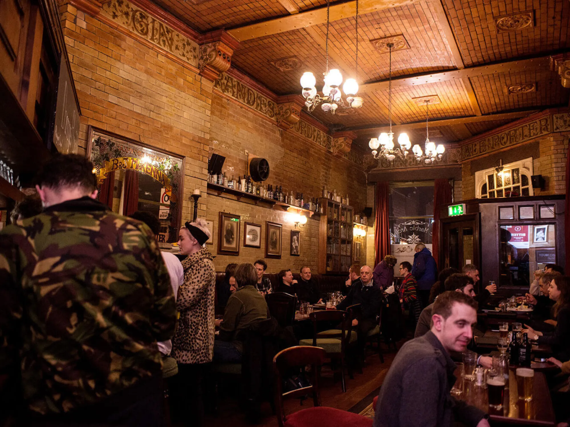 A busy, chandelier-lit room with tiled walls and a decorated ceiling at The Marble Arch, a pub in the Northern Quarter, Manchester
