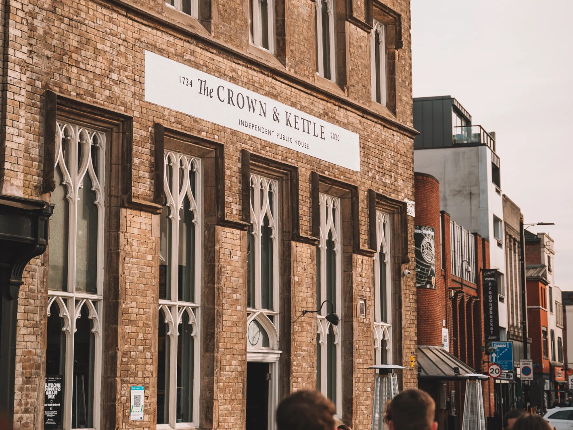 The Gothic brick front of The Crown & Kettle with drinkers outside, a pub in Ancoats, Manchester