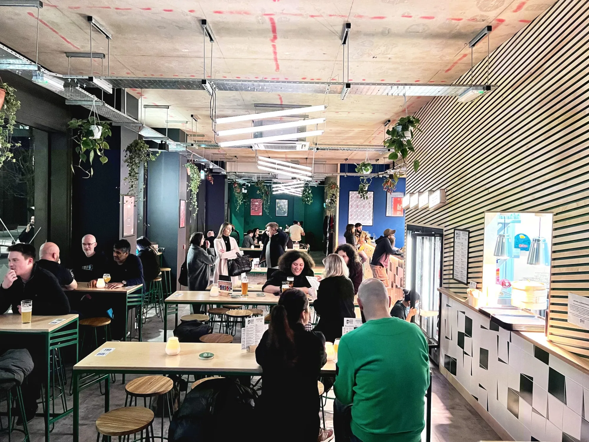 A busy North Taproom at Circle Square, with tables, green tiles and hanging plants, a brewery taproom in Oxford Road, Manchester