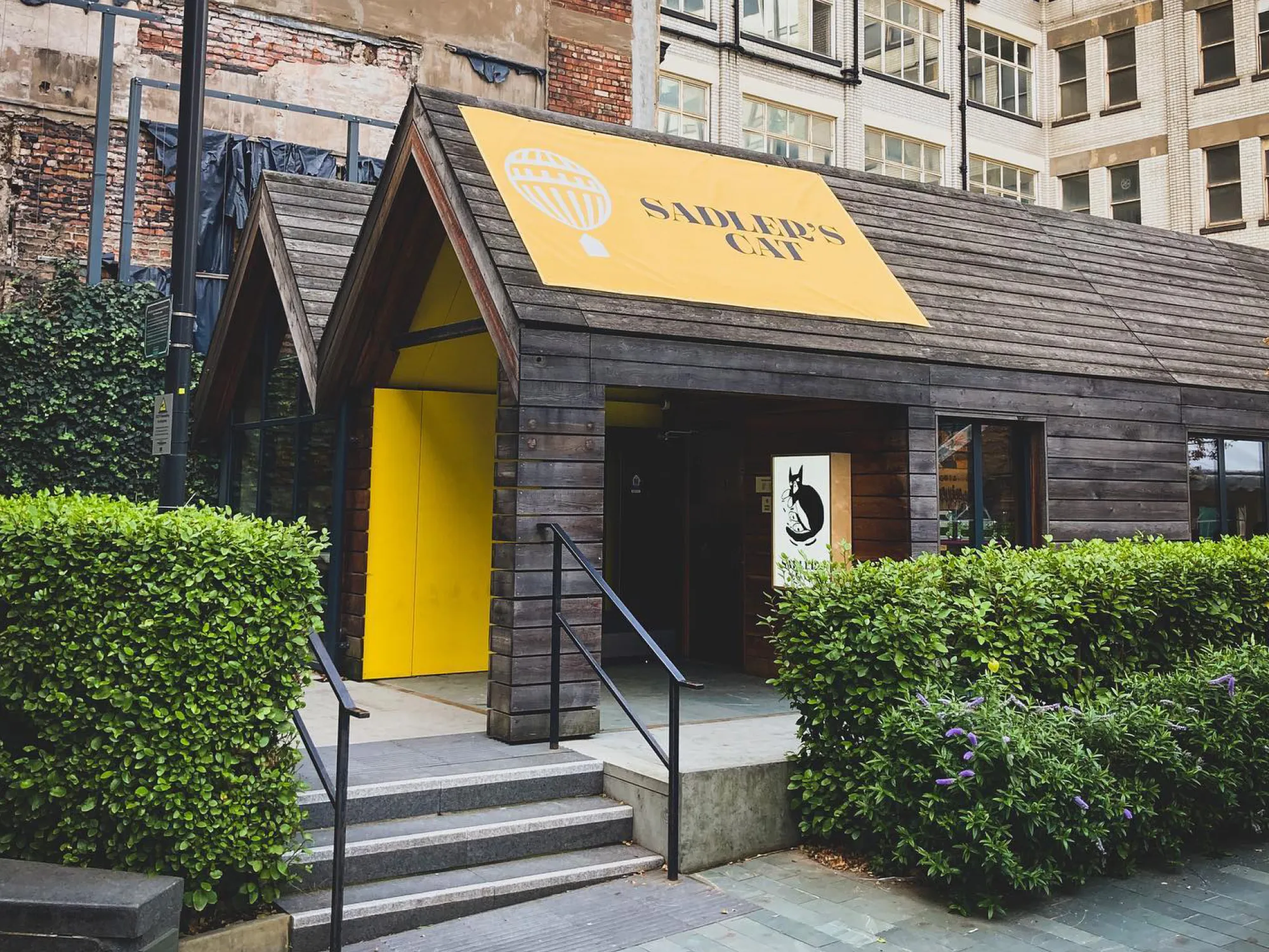 The timber front of Sadler's Cat in Sadler's Yard, with its yellow sign and door, a pub in the Green Quarter, Manchester
