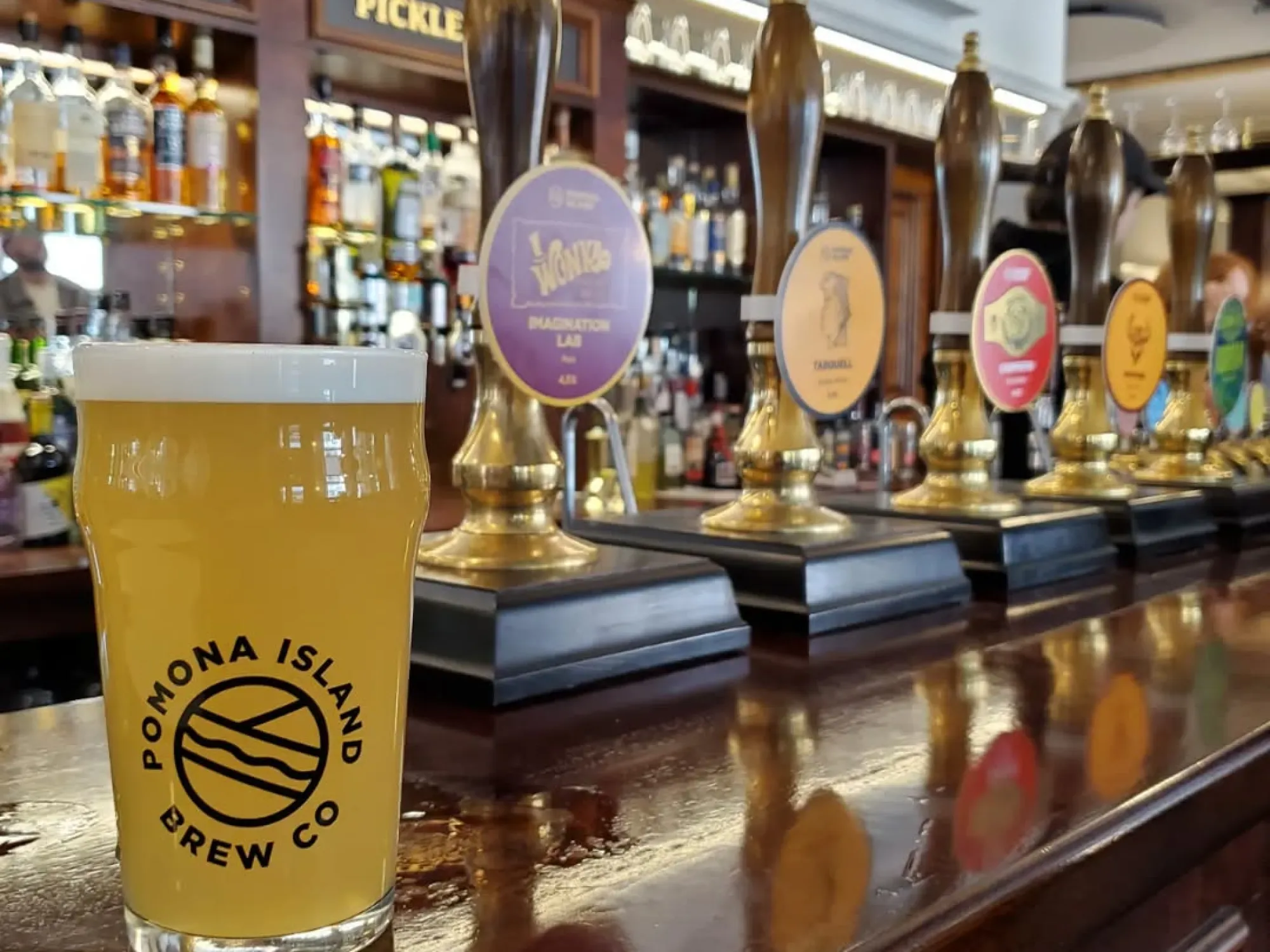 The bar at North Westward Ho, with its row of handpumps and a pint of Pomona Island in front, a pub in Deansgate, Manchester