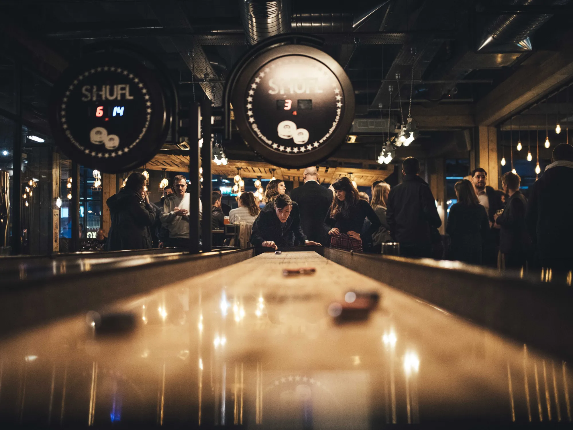 Inside Gasworks Brew Bar, looking down the shuffleboard table to a busy bar, a brew pub in First Street, Manchester