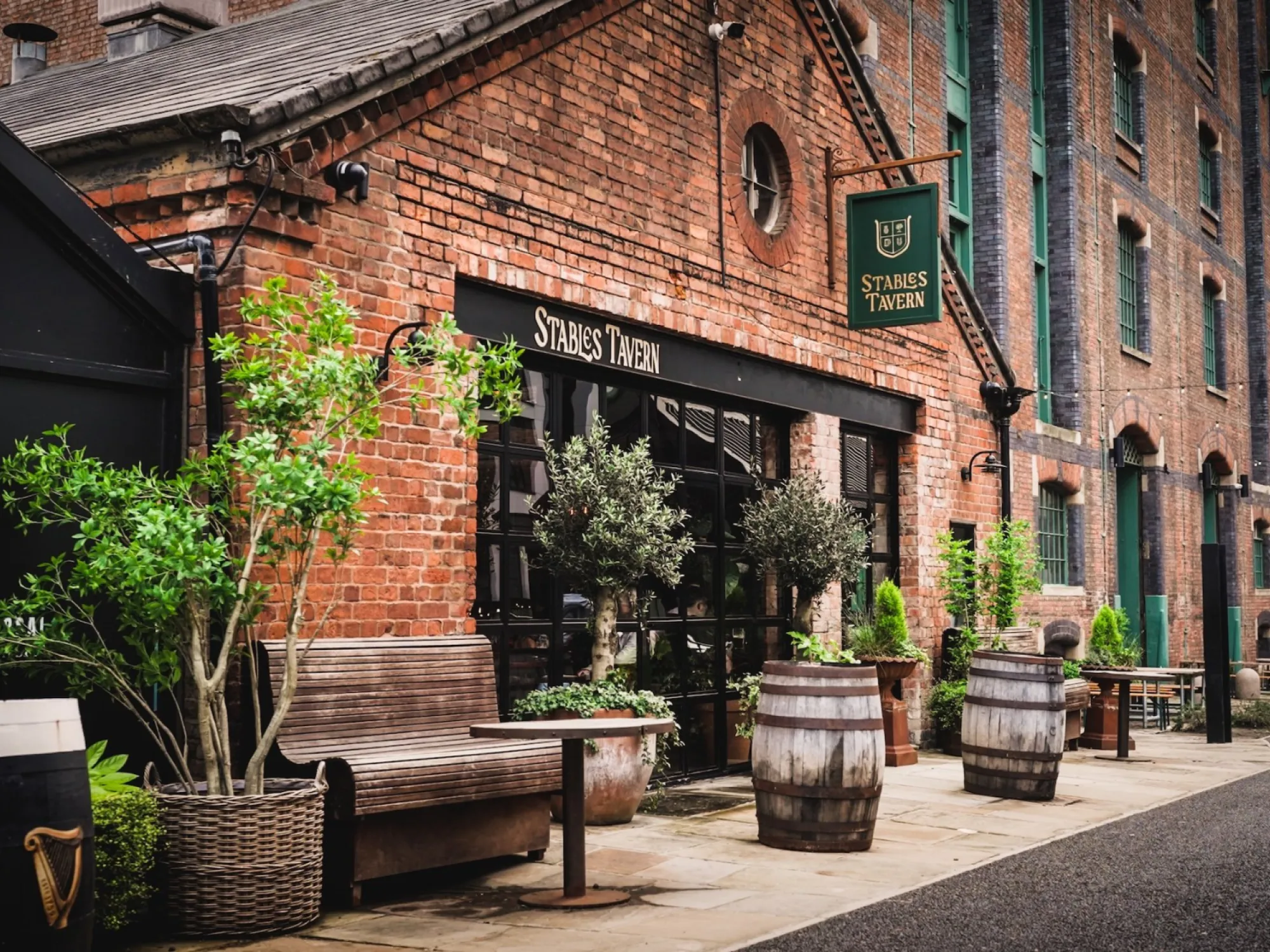 The red brick front of the Stables Tavern on Grape Street, with barrels, benches and planters outside, a pub in St John's, Manchester