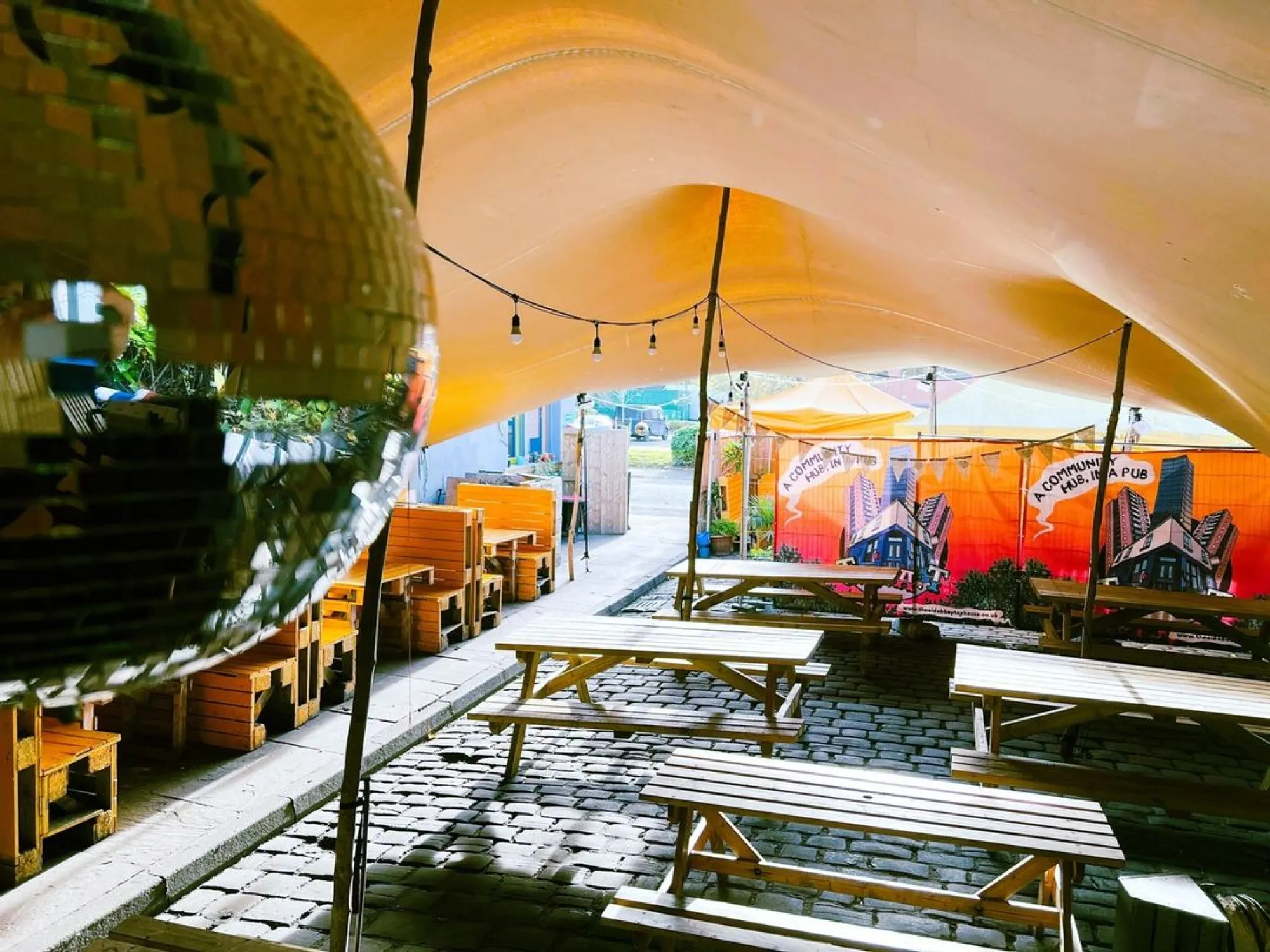 The covered beer garden at The Abbey, with picnic benches under a canopy and a mirror ball, a pub in Hulme, Manchester