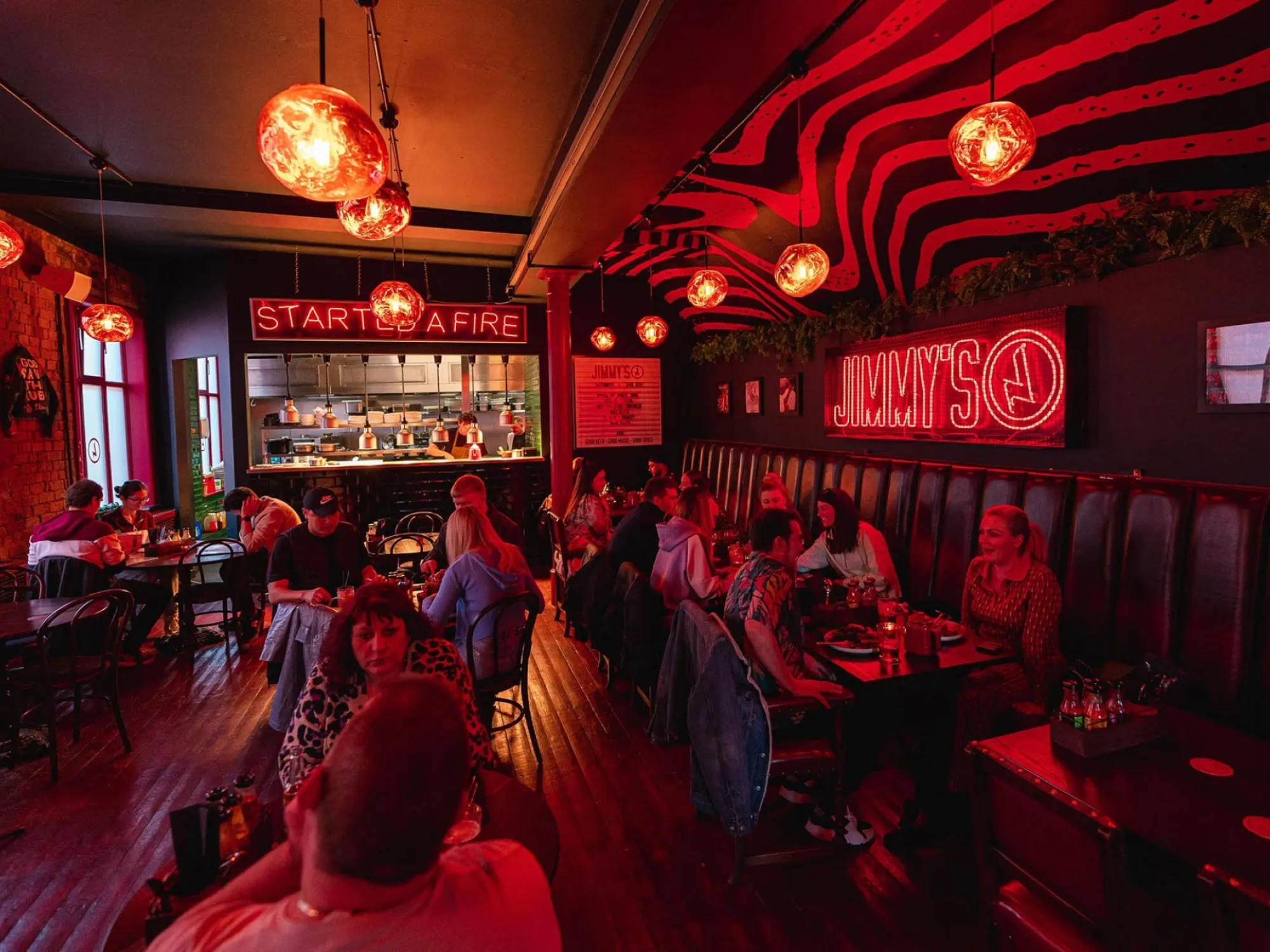 Diners at tables and red leather booths under glowing lamps and a neon sign at Jimmy's, a craft beer bar in Ancoats, Manchester