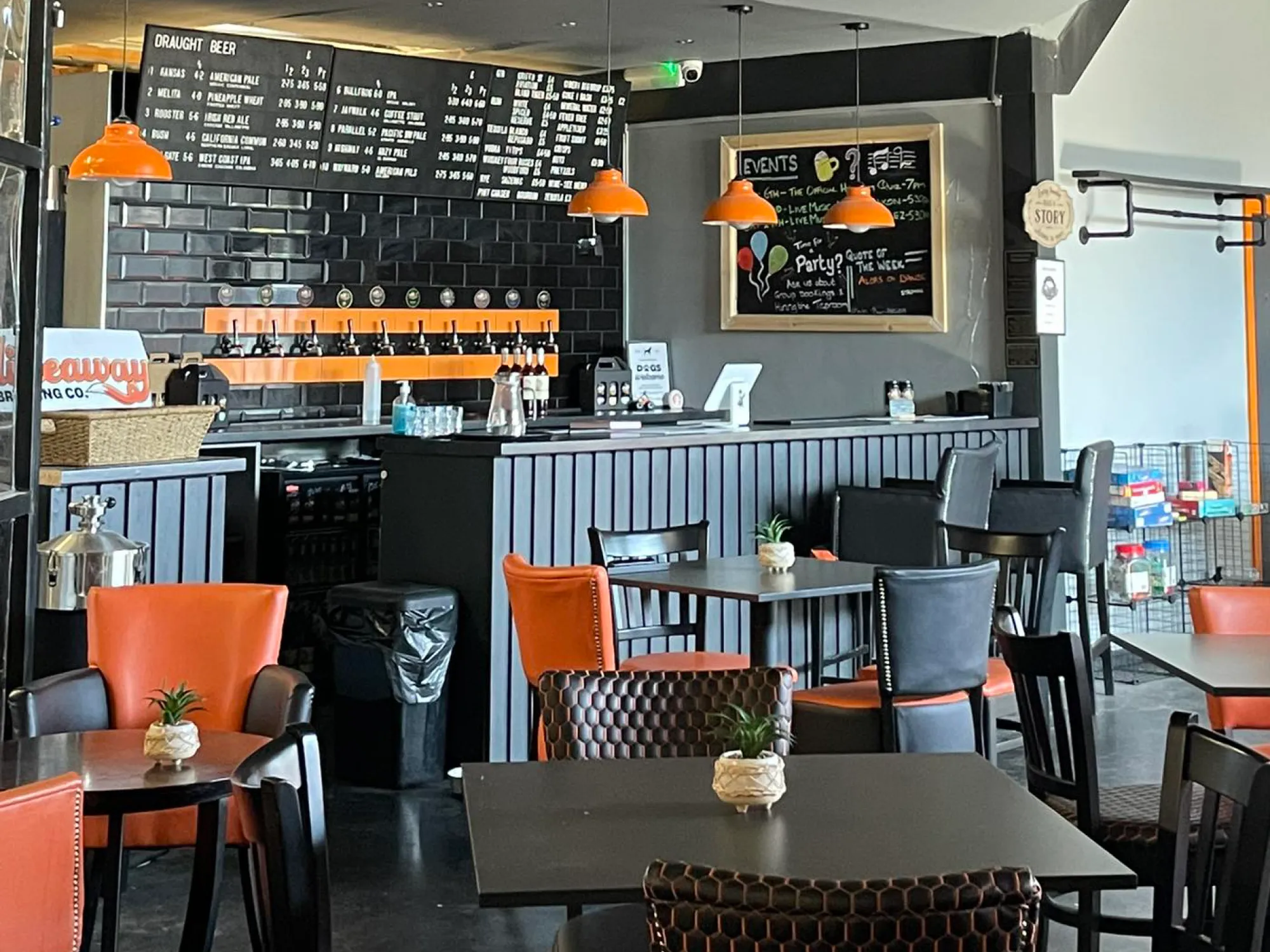 The taproom at Hideaway, with orange chairs, tables and the bar under its chalkboard menus at Hideaway Brewery Tap, a brewery taproom in Salford Quays