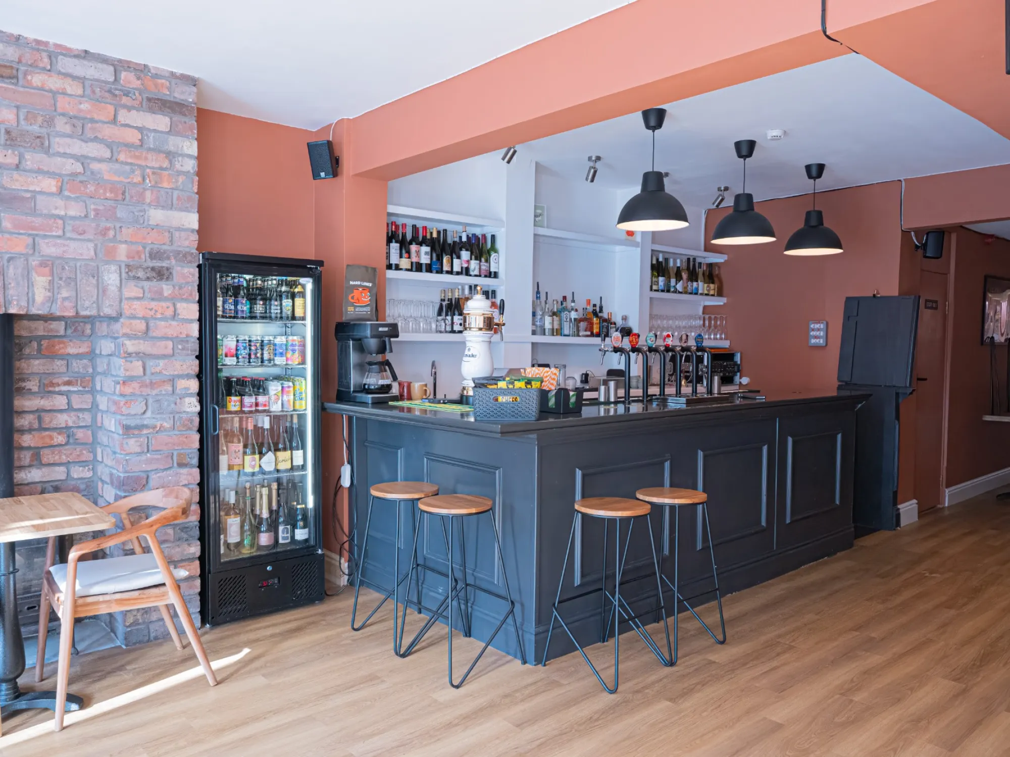The bar at Plere, with bar stools, a drinks fridge and terracotta walls, a craft beer bar in Chorlton, Manchester