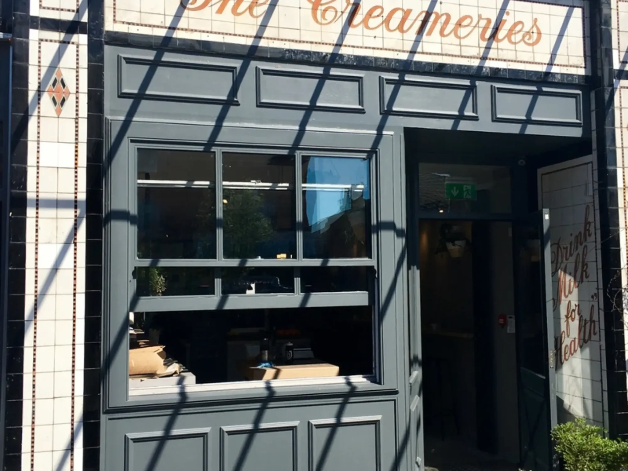 The grey painted shopfront of the Creameries on Wilbraham Road, with its tiled sign above the door, a craft beer bar in Chorlton, Manchester