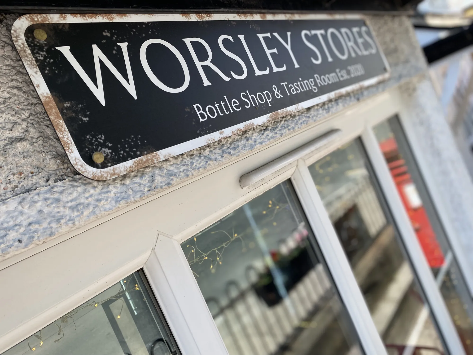 The Worsley Stores sign above the shop front window, reading Bottle Shop and Tasting Rooms, a craft beer bottle shop in Worsley, Manchester