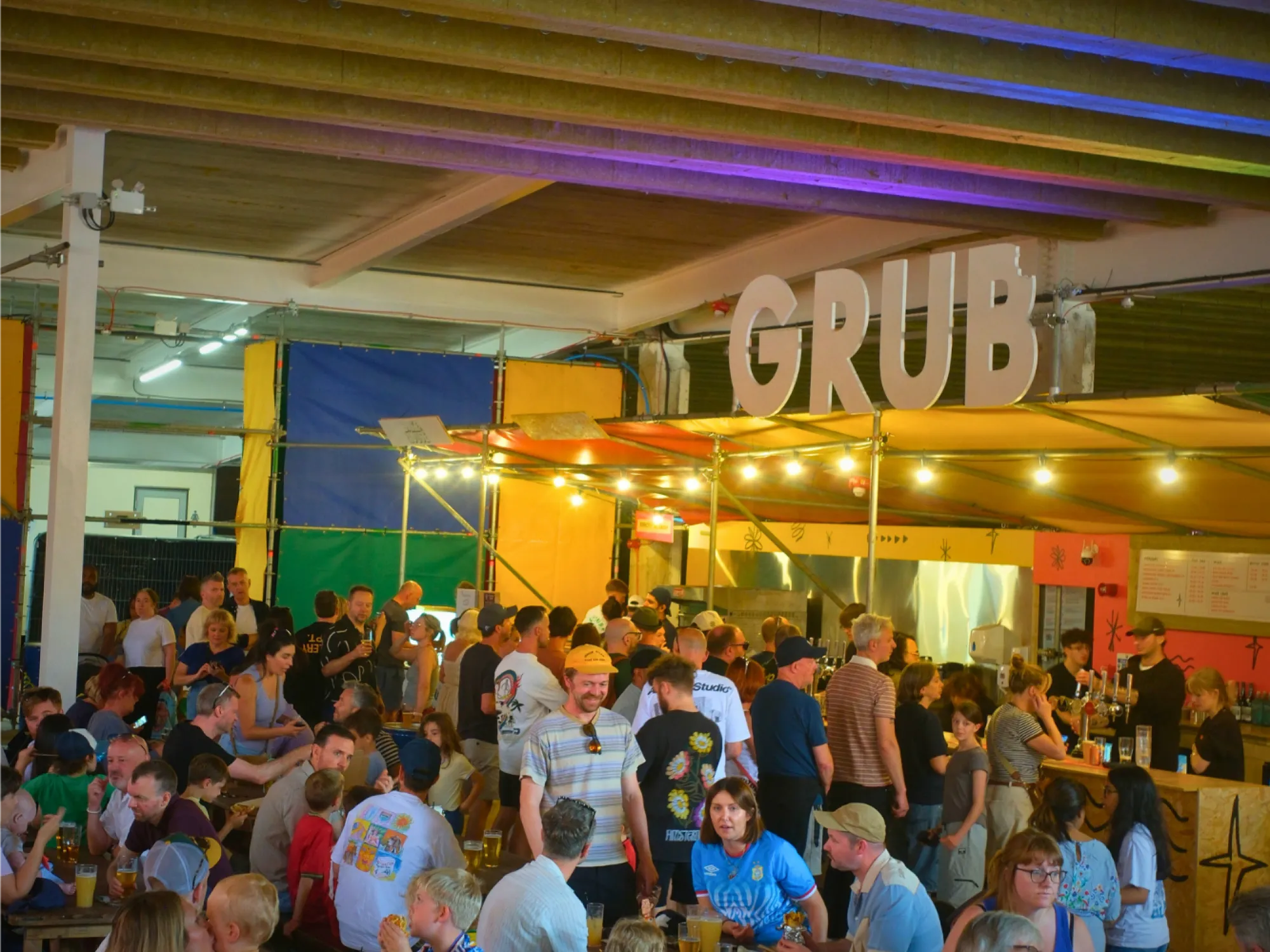 GRUB Stretford under the multi-storey car park, with its sign, colourful stalls and busy tables, a street food hall in Stretford, Manchester
