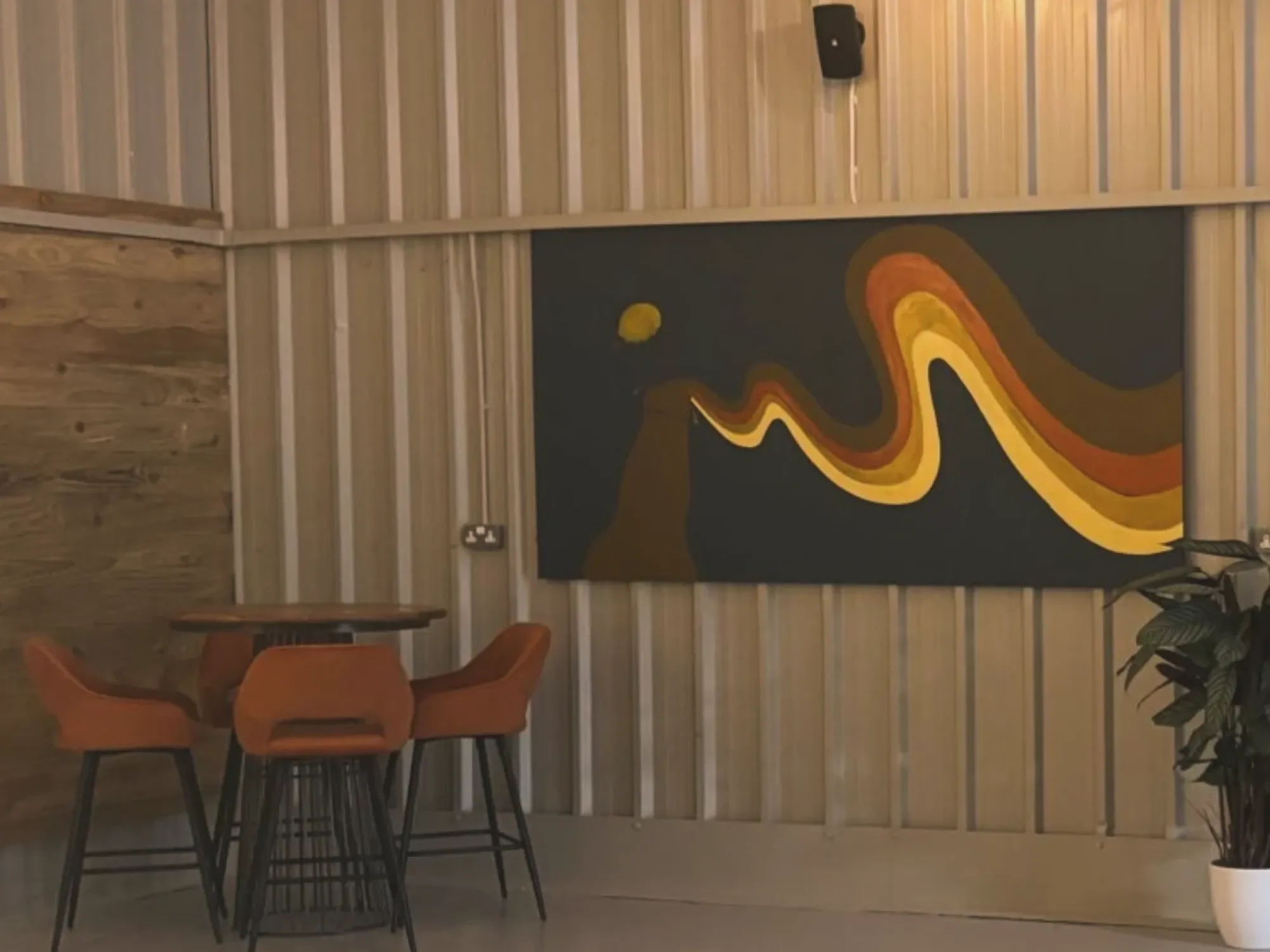 Orange high stools and a table beneath a wave mural inside Guest in Stalybridge, a craft beer bar in Stalybridge