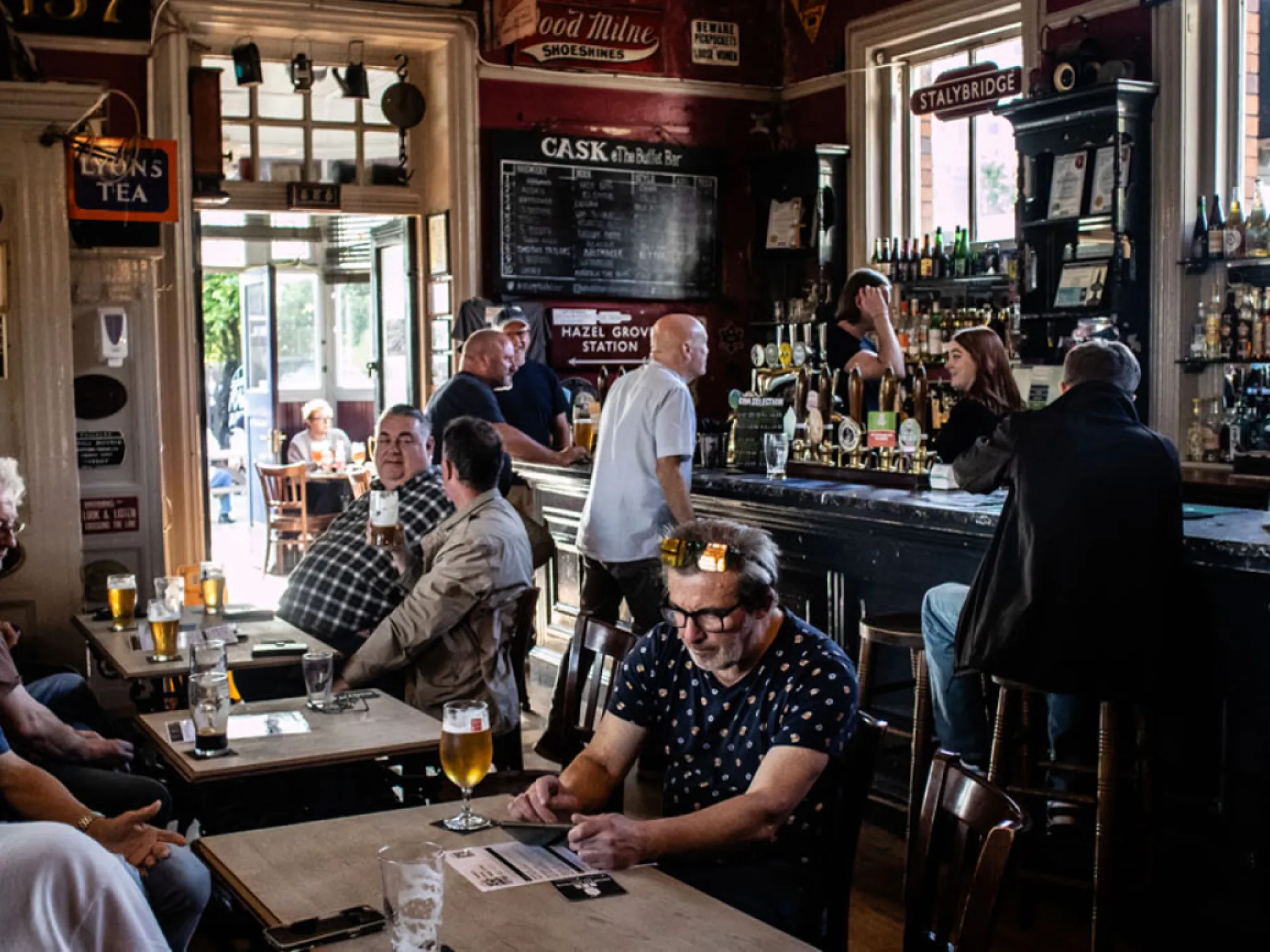 The bar room at Stalybridge Buffet Bar, with railway signs, a busy bar and drinkers at tables, a pub in Stalybridge