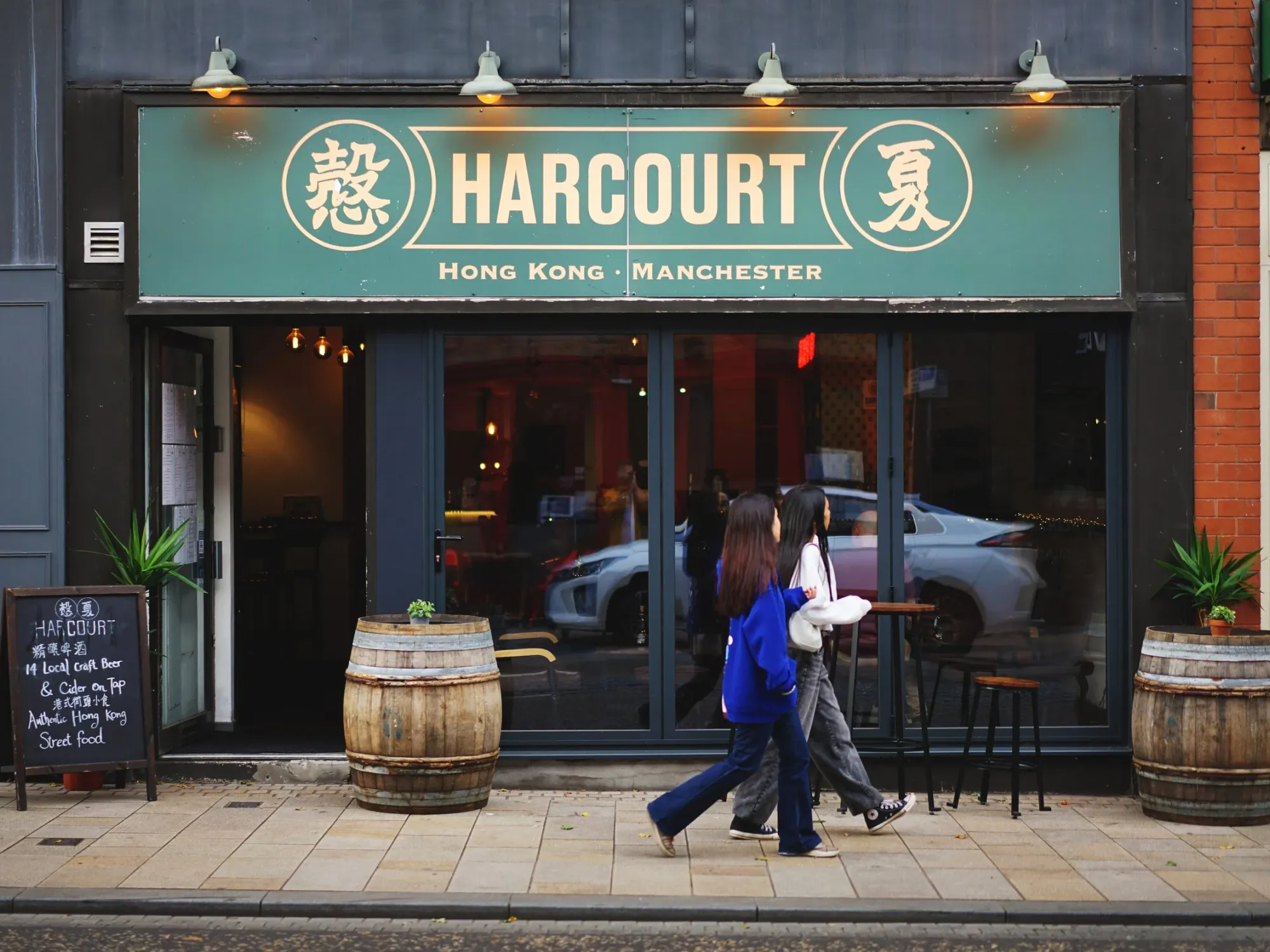 The green Harcourt fascia and glass front on Stamford New Road, Altrincham, with barrels outside, a pub in Altrincham