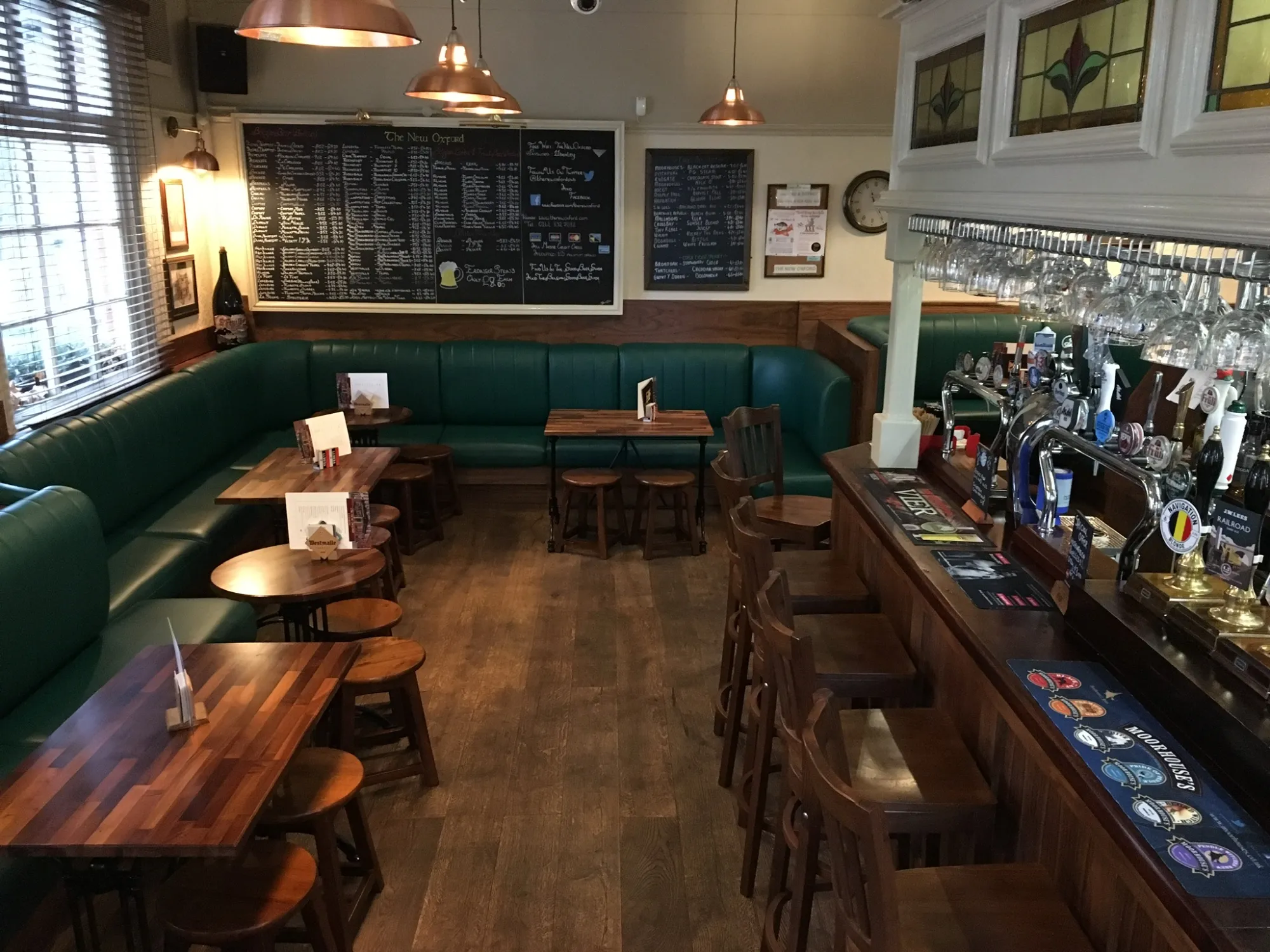 The bar room with green banquettes, the long bar and its handpulls, and the beer boards at The New Oxford, a pub in Salford