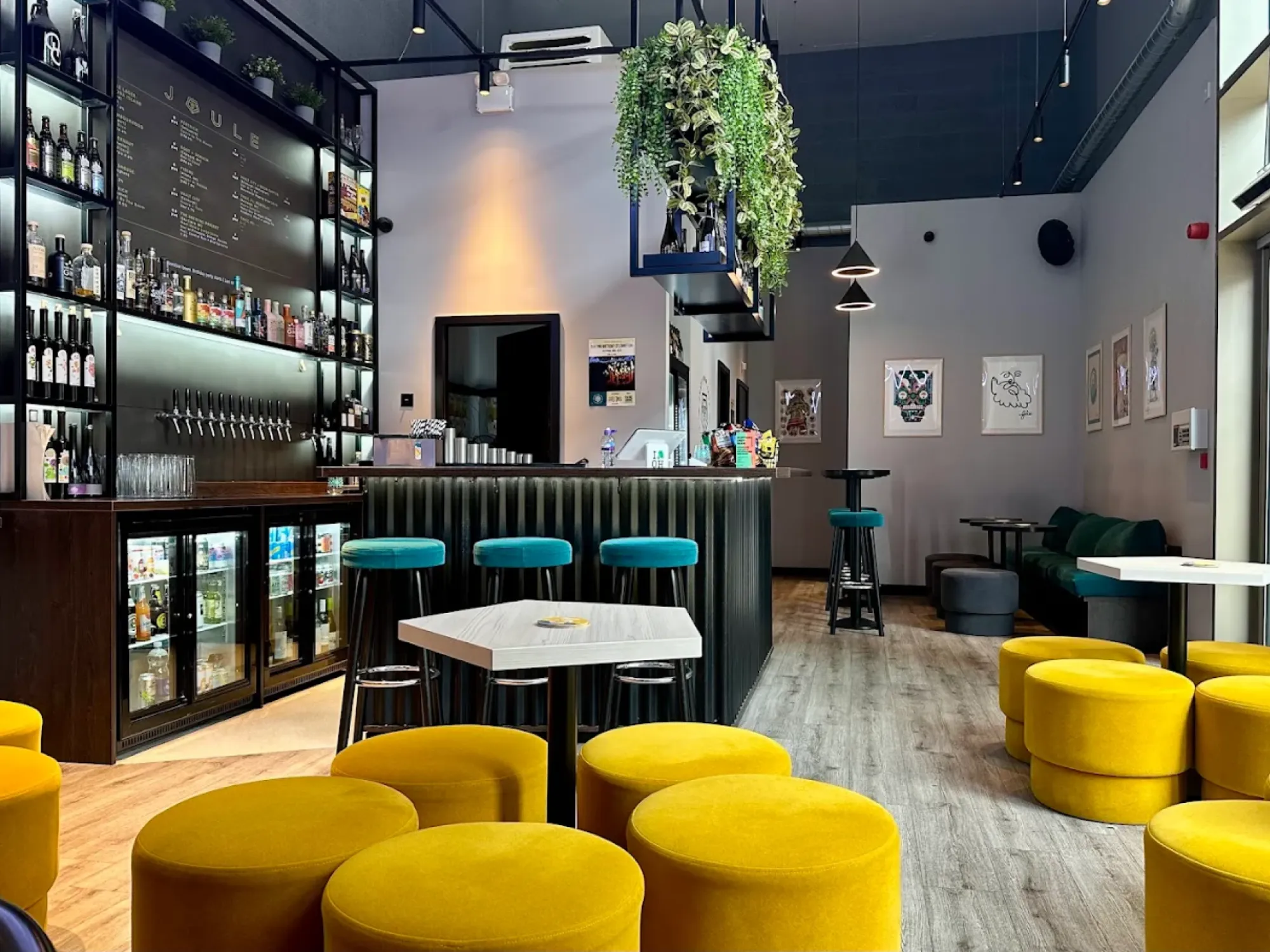 The bar and bottle shelves with fridges, high tables and mustard velvet stools at Joule, a craft beer bottle shop in Salford