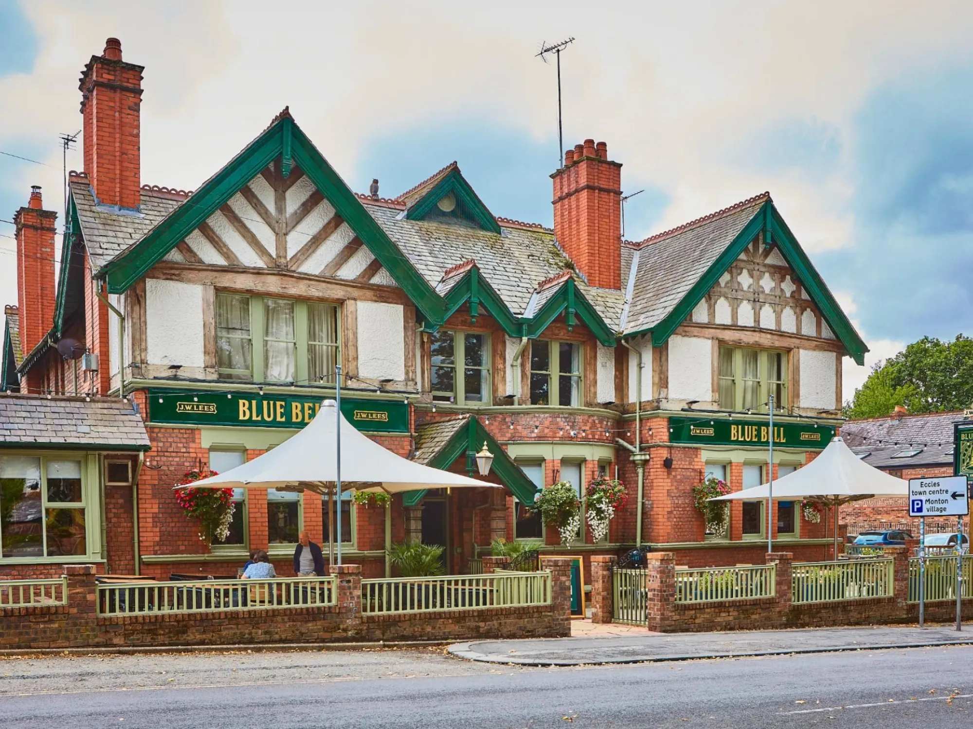 The mock-Tudor front of the Blue Bell on Monton Green with its green gables and front terrace, a pub in Eccles