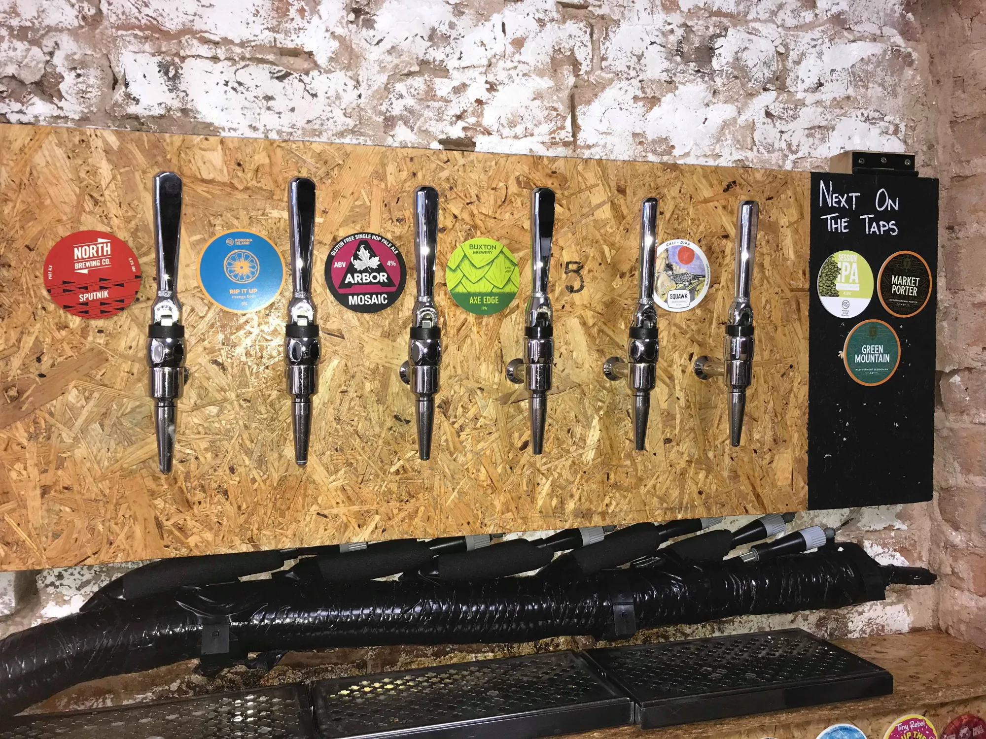 The row of keg taps on a chipboard panel against a whitewashed brick wall at Northern Type, a craft beer bottle shop in Eccles