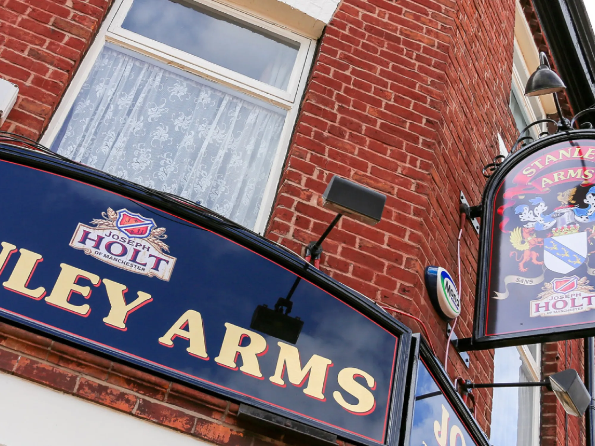 The Stanley Arms name board and Holt hanging sign on the red-brick front of the pub, a pub in Eccles