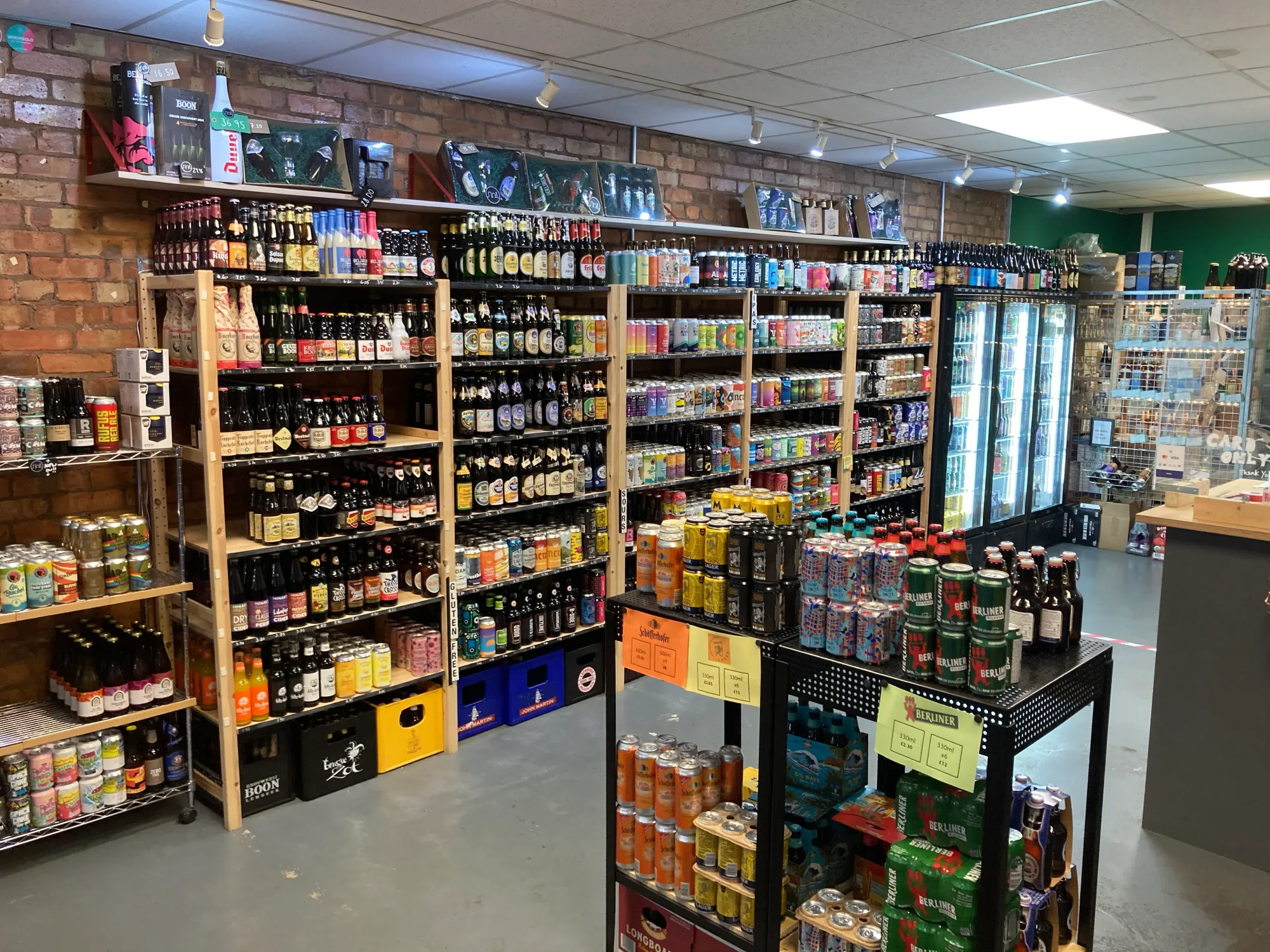 Inside the Prestwich shop: brick walls lined with beer shelves, can stands and fridges at Keg, Cask & Bottle, a craft beer bottle shop in Prestwich